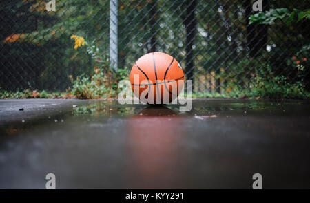 Close-up of ball on wet basketball court against chainlink fence Stock Photo