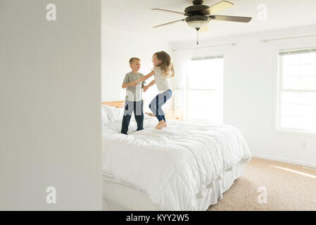 Siblings holding hands while jumping on bed Stock Photo