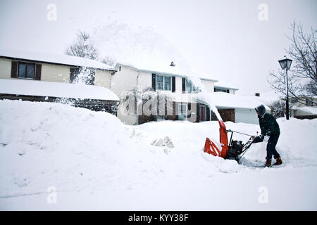 Side view of man using snowblower in front of houses during winter Stock Photo