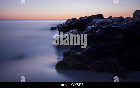 Sunset serenity: Long exposure captures silky waters, black rocks, and a twilight sky—a perfect blend of motion and tranquillity. Stock Photo