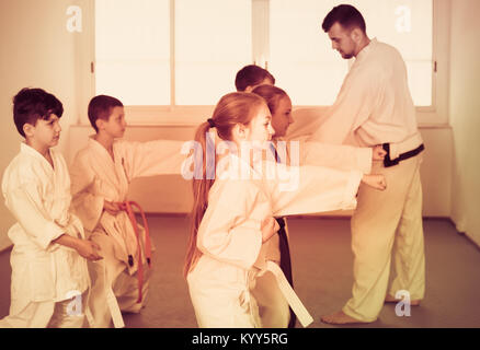 Young children practice karate kicks with male coach during karate class Stock Photo