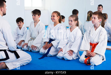 Young smiling man training new karate moves with children during class. Focus on boy Stock Photo