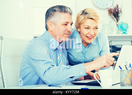 Smiling colleagues look interesting information on internet on laptop at desk at ofice Stock Photo
