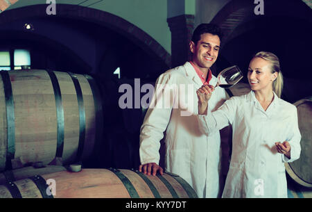 Friendly smiling  specialists in white robes checking ageing process of wine Stock Photo
