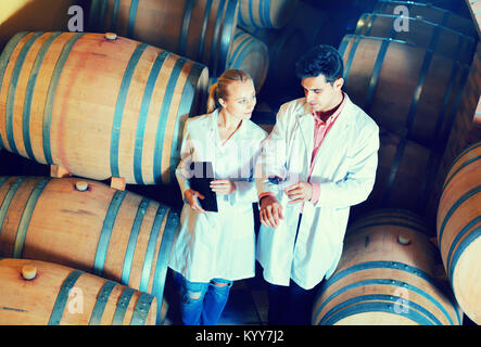 Friendly specialists in white robes checking ageing process of wine Stock Photo