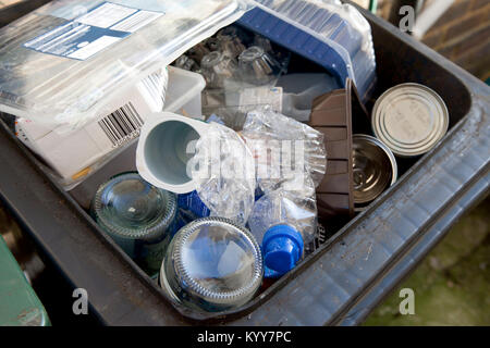 Wheelie bin full of domestic recycling waste, glass bottles, tin cans and plastic bottles, plastic waste, Recycling. Stock Photo