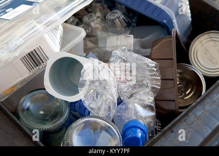 Wheelie bin full of domestic recycling waste, glass bottles, tin cans and plastic bottles, plastic waste, Recycling. Stock Photo