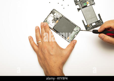 Man doing adjustments and repairs to his smartphone using a precision screwdriver in a close up view of his hands and the disassembled mobile phone on Stock Photo