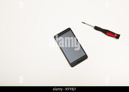 Studio shot high-angle view close-up of precision screwdriver and a smartphone in a concept of screen replacement, repairs and maintenance over white  Stock Photo