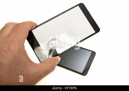 Man holding a shattered smartphone screen in his hand with the mobile phone visible below in a close up view showing the damage to the glass Stock Photo