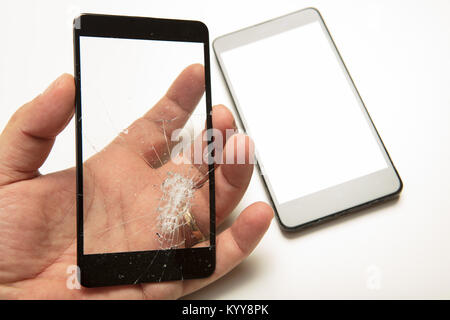 Man holding a shattered smartphone screen in his hand with the mobile phone visible below in a close up view showing the damage to the glass Stock Photo