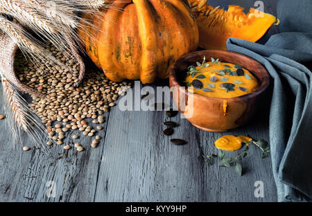 Pumpkin and lentil creme soup served in olive wood bowl with thyme leaves and pumpkin seeds on dark rustic wooden table, with ingredients around. Stock Photo