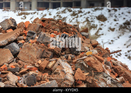 A pile of construction debris with broken bricks and concrete in winter against a background of snow. Stock Photo