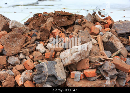 A pile of construction debris with broken bricks and concrete in winter against a background of snow. Stock Photo