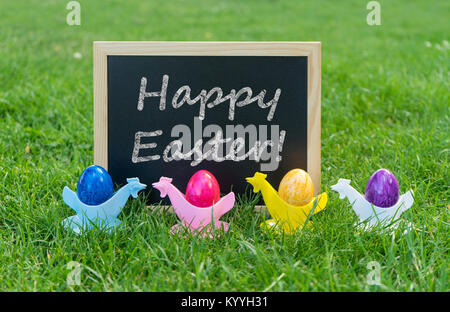 Eastercard with chalkboard and colorful Easter eggs in egg cups on a meadow Stock Photo