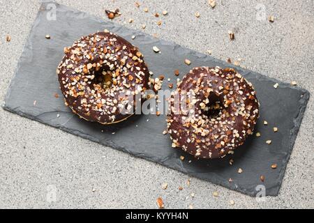 Top down view on two donut with cocolate and chopped almonds lying on slate stone serving plate Stock Photo