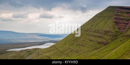 A lone walker stands on the summit of Fan Brycheiniog overlooking Llyn y Fan Fawr galcial lake in the Brecon Beacons of South Wales UK Stock Photo