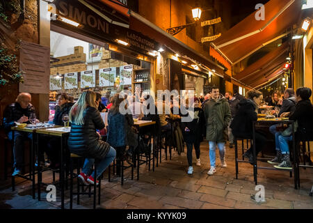 People sitting out eating and drinking in restaurants, cafes and bars in Via Pescherie Vecchie, a street in Bologna city, Italy at night Stock Photo
