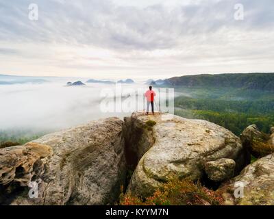 Photographer on the crater. Man on peak above thick cloud, dark rainy weather within mountain trail. Stock Photo