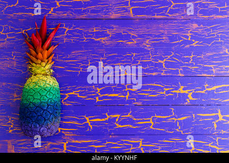 Brightly colored pineapple in rainbow colors forming a side border on a wooden background with cracked blue paint texture and copy space Stock Photo