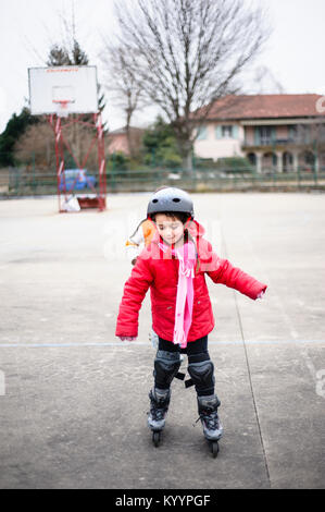 little girl learns to skate with rollerblading at the basketball court on a winter day Stock Photo