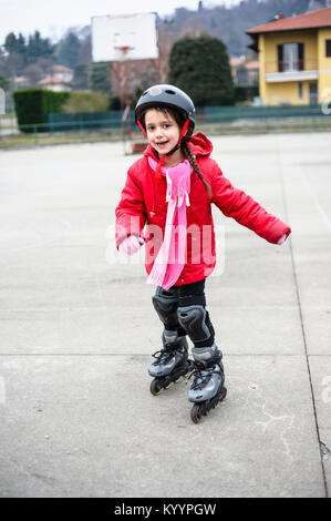 little girl learns to skate with rollerblading at the basketball court on a winter day Stock Photo