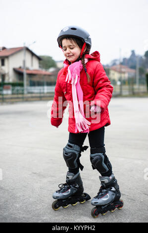 little girl learns to skate with rollerblading at the basketball court on a winter day Stock Photo