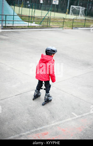 little girl learns to skate with rollerblading at the basketball court on a winter day Stock Photo