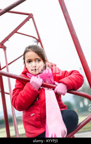 little girl climbs on iron frame of a basketball hoop in an outdoor basketball court Stock Photo