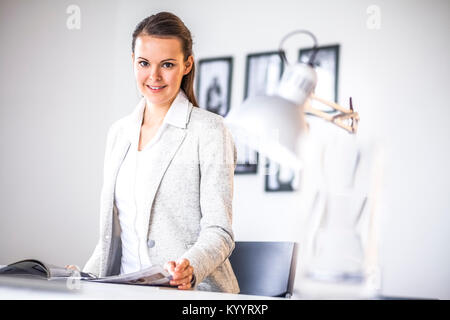 Portrait of confident young businesswoman analyzing brochure at desk in office Stock Photo