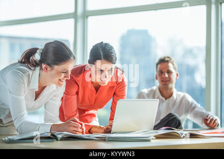 Smiling young businesswomen using laptop with male colleague in background Stock Photo