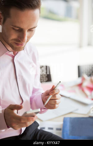 Young businessman text messaging through mobile phone in creative office Stock Photo