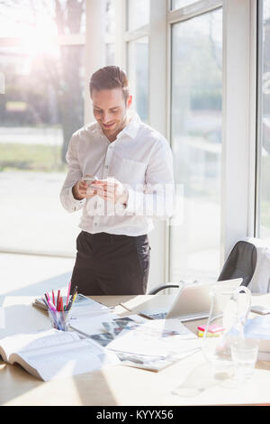 Smiling young businessman text messaging through mobile phone in creative office Stock Photo