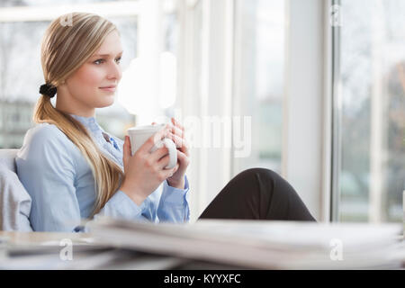 Thoughtful young businesswoman having coffee in office Stock Photo
