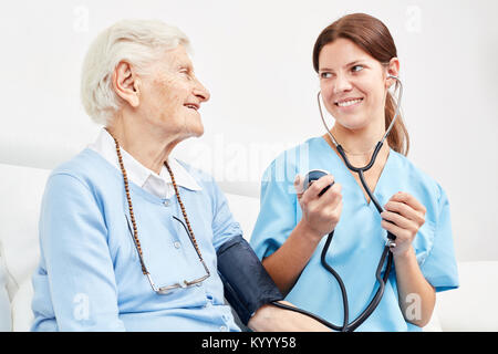 Young caregiver makes a blood pressure measurement at senior woman as a precaution at home Stock Photo