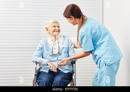 Caring caregiver taking care of a smiling elderly woman in a wheelchair Stock Photo