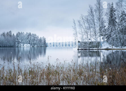 Winter landscape with sauna cottage and peaceful lake at evening in Finland Stock Photo