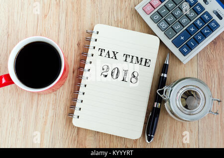 Tax Time text on notepad - coffee, jar coins, pen and calculator on top of wooden table. Stock Photo