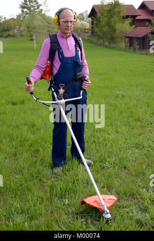 Man wearing ear protectors and glasses mowing grass with petrol weed trimmer Stock Photo