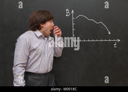 Man looks at the graph with bitcoin falling down Stock Photo