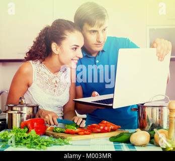 Happy russian couple with vegetables and laptop in domestic kitchen Stock Photo
