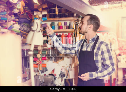 Young man worker examining threads for sewing in leather workshop Stock Photo