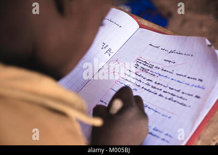 Over shoulder top view of a child or schoolkid writing in french in his workbook in a school located in the slums of Ouagadougou, Burkina Faso. Stock Photo