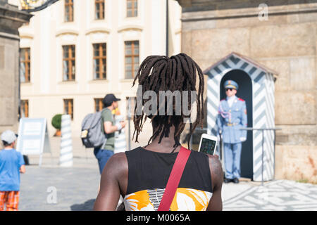 PRAGUE - AUGUST 29: Black woman in selective focus from behind with dreadlocks lifts mobile to yake photo of Guards Prague Castle Guard in blue unifor Stock Photo