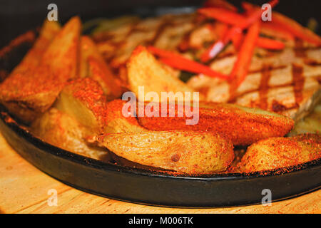 Pork steak with fried potatoes and onions on a cast-iron brazier Stock Photo