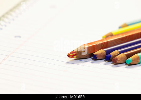 Seven wooden color pencils next to each other on a paper sheet of a notebook with spiral. Stock Photo