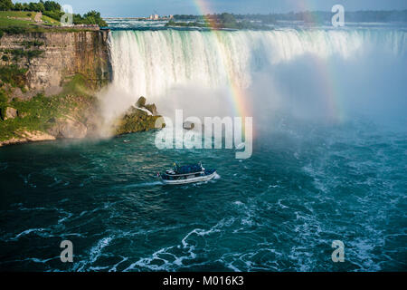 A tour boat approaching the horse shoe falls also known as the lady of the mist of Niagara falls through a rainbow streak Stock Photo