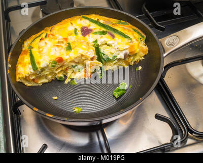 A Frittata made with eggs and vegetables cooked in the oven on a skillet  pan  cut in half for serving on the gas hob Stock Photo