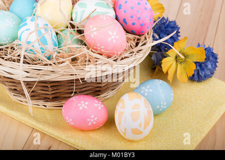 Three colored Easter eggs in front of a basket of eggs Stock Photo