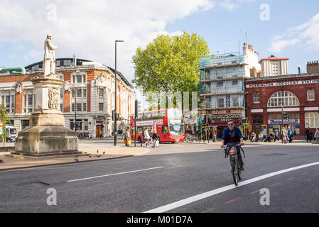 London, UK - April 2017. Cyclist on Santander bike and people walking plus red bus in the background in front of Mornington Crescent Underground Stati Stock Photo